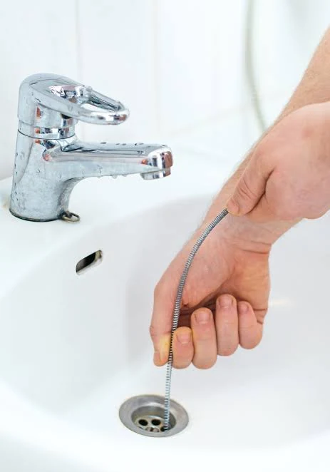 A flexible drain-cleaning cable being used to clear a blocked bathroom sink